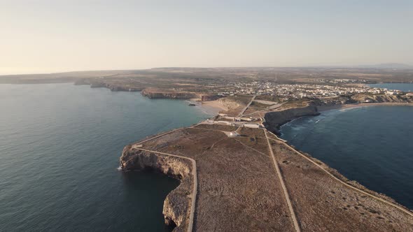 Fly over narrow headland towards Sagres Fortress, Algarve, Portugal. Sunset wide shot