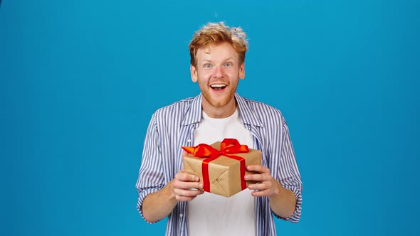 Young Redhead Man Catches Paper Gift Box with Red Ribbon