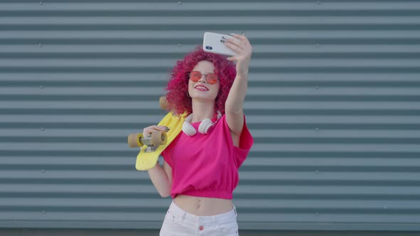 A Pink Curly Teenager is Recording Video Blog with Smartphone Outdoors