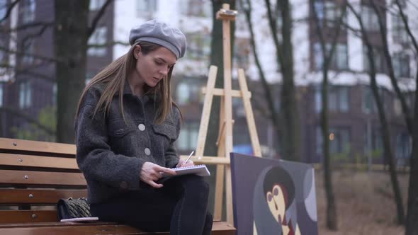 Concentrated Skilled Woman Drawing Sketch with Picture at Easel at Background