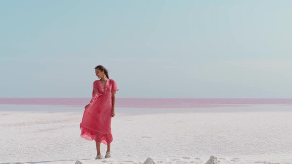 Happy Carefree Elegant Woman in Blowing Pink Dress Enjoys Her Vacation While Walking Along White