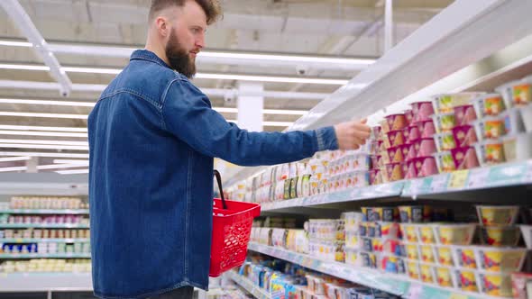 Male Shopper is Choosing Yogurt for Breakfast and Lunch Shopping in Supermarket