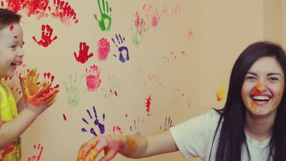 Happy Mother and Her Cute Boy Having Fun Together Leaving Their Colorful Handprints on the Wall