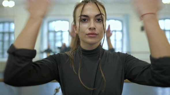 Confident Young Brunette Woman Moving Hands Rehearsing Dance in Studio Indoors with Blurred People