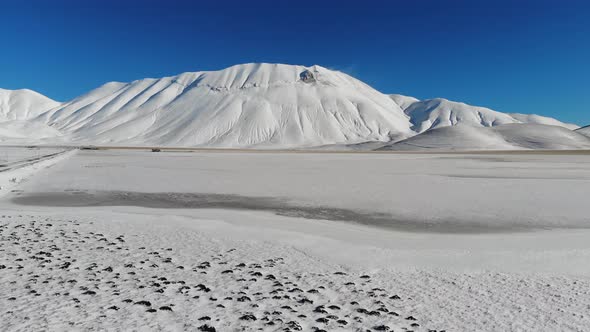 Drone flight over frozen landscape towards Piano Grande, Castelluccio