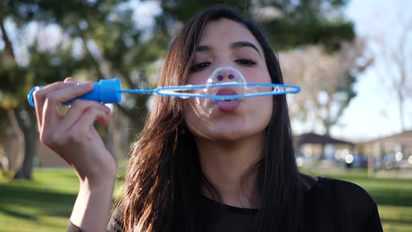 Close up of a happy young woman playing and smiling while blowing bubbles in the dreamy park sunligh