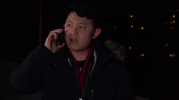 A Young Asian Man Talks on a Smartphone in an Urban Area at Night