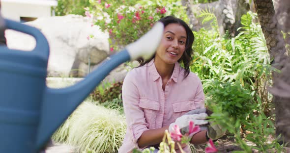 Happy biracial woman gardening, planting flower while her partner watering plants