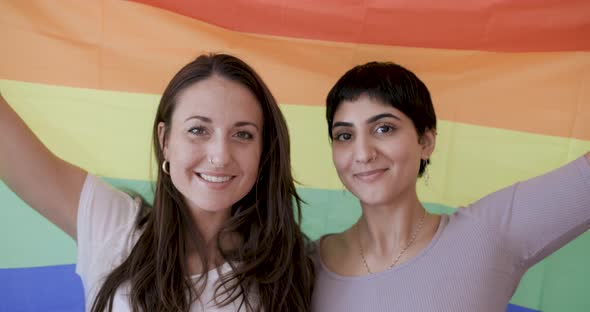 Happy girl friends lesbian couple holding a pride rainbow flag on background