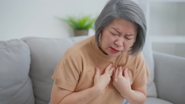 Asian daughter help senior mother having chest pain from heart attack.