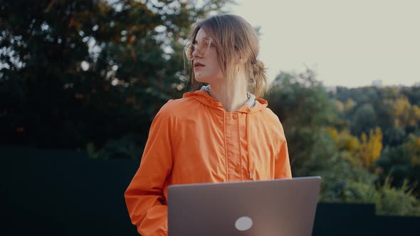 Tired Young Woman with Laptop in Her Arms Looking in Parts and Admiring Nature in the Park