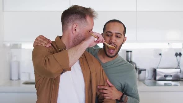 Multi ethnic male same sex couple preparing food and tasting in kitchen