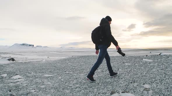 Man Photographer with Camera Walking on Snow Desert in Iceland