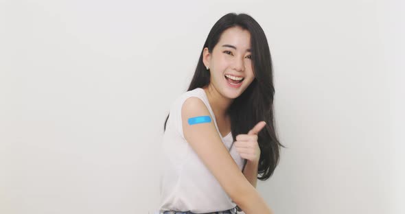 Asian Woman Shows Thumb Up And  Bandage On Arm. Happy Asian Woman Feels Good After Received Vaccine.