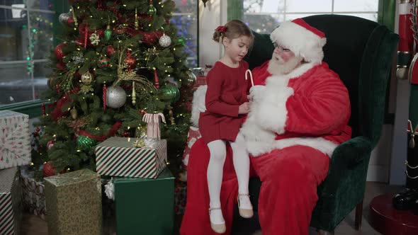 Santa Claus gives girl a candy cane as she sits on his lap