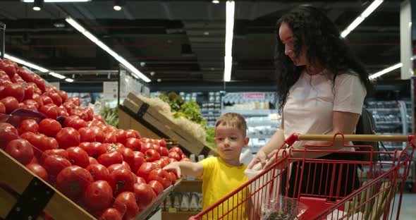 Cute Woman with Her Little Happy Son Chooses Fresh Vegetables Together at the Grocery Store