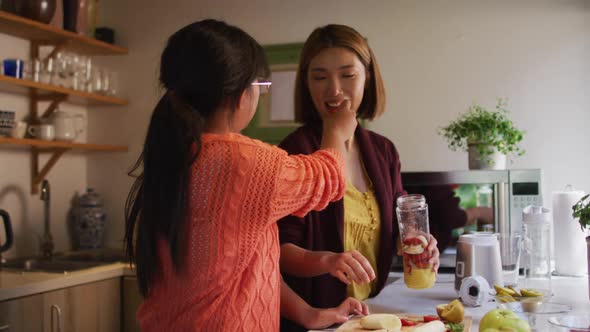 Asian mother and daughter preparing healthy drink in kitchen smiling