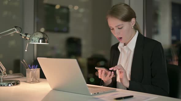 Upset Businesswoman Scrolling on Cellphone in Office at Night