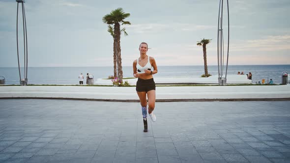 Sportive Girl with Prosthesis Training Outdoors at Seaside Running to Camera