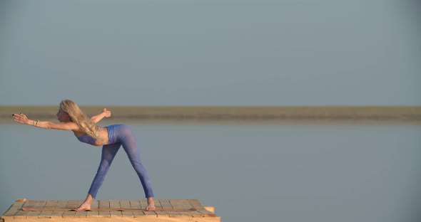 Woman with Blonde Hair is Stretching and Doing Yoga on the Lake Sunset