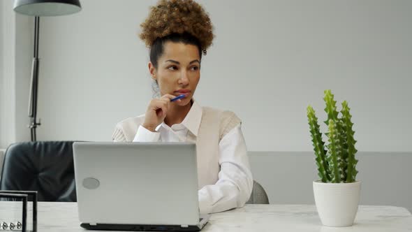 Portrait of a Smiling Thoughtful Woman Sitting at an Office Desk with a Laptop