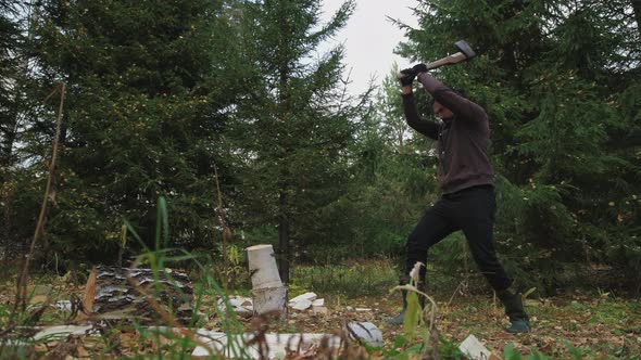 Young handsome man chops wood in the forest. 