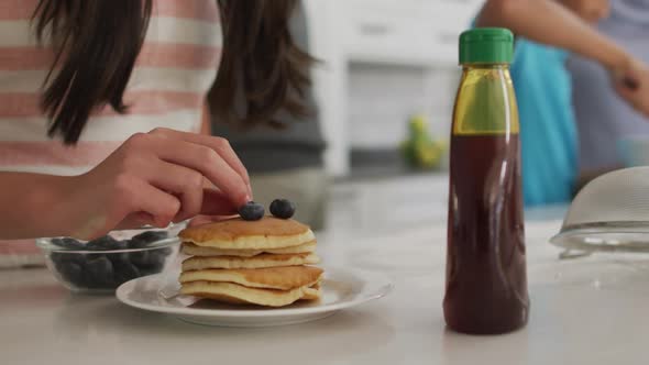 Midsection of brother and sister in kitchen, sister putting berries on stack of pancakes