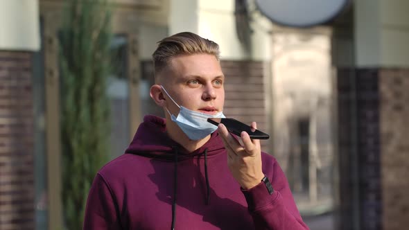 Portrait of Young Man in Lowered Medical Mask Is Talking on Her Smartphoneis Over the Speakerphone