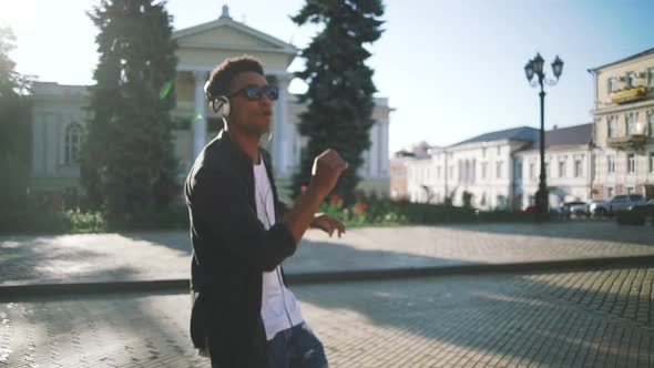 Young Stylish Hipster Black Man in White Headphones and Sun Glasses Dancing Outdoor in City Centre