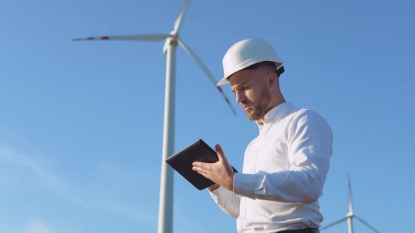 A Male Engineer in a White Helmet and a Classic Shirt Inspects the Power Plant's Capacity and Makes