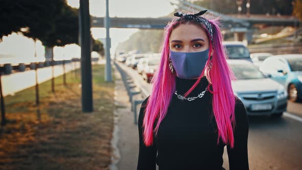 Lady Hipster in Informal Outfit and Protective Mask is Looking at you Posing at Embankment By City