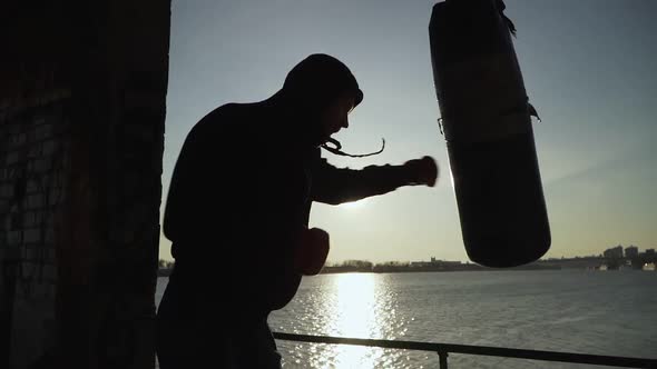 A silhouette of a boxer who hits the punching bag. Against the background of the sunset.