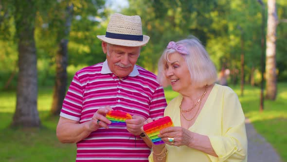 Stylish Senior Grandmother Grandfather Playing Squeezing Antistress Toy Simple Dimple Game in Park