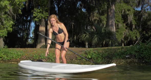 A young woman walking to the edge of a lake to go sup stand-up paddleboarding.