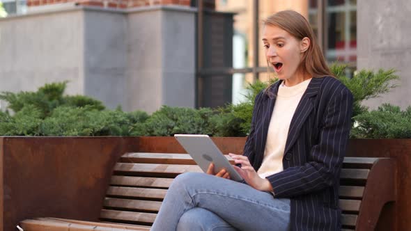 Woman Sitting on Bench Celebrating Success of Project on Tablet