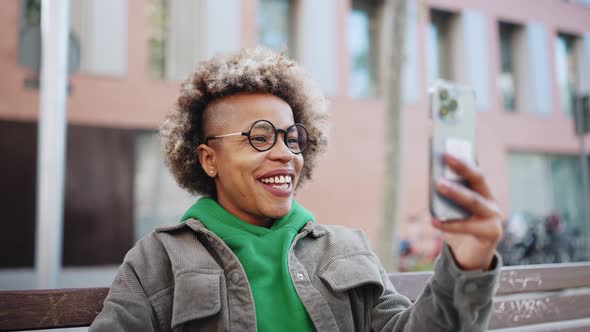 Smiling African woman wearing green hoodie talking by video call on smartphone
