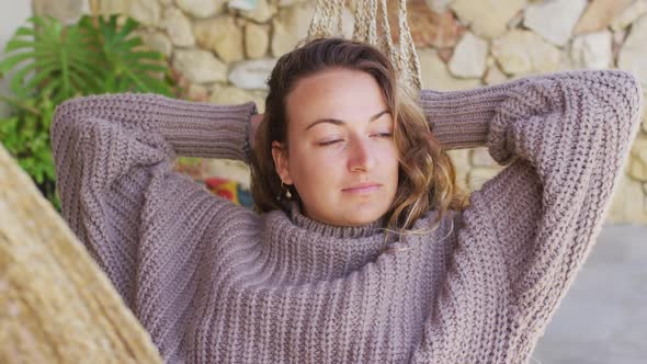 Smiling caucasian woman lying in hammock relaxing and enjoying the view from sunny garden patio