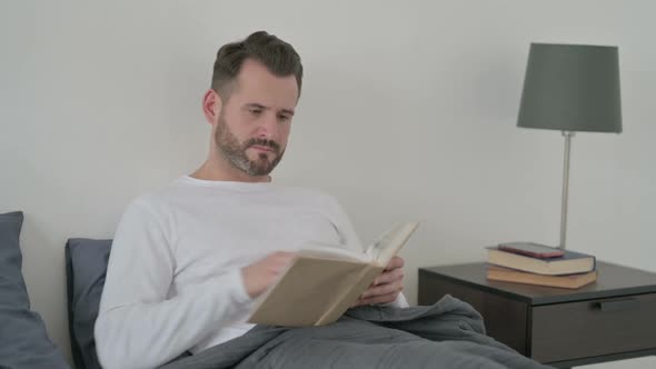 Man Reading Book While Sitting in Bed