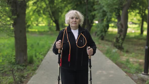 Active Senior Old Woman Training Nordic Walking with Ski Trekking Poles in Park