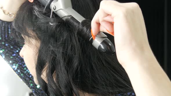 A Beautiful Spectacular Young Woman Winds Her Long Black Hair on a Special Iron to Create Curls