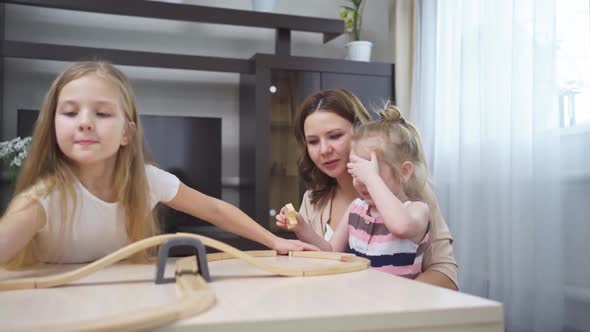 Mom and Daughters Play with Wooden Toy Railway