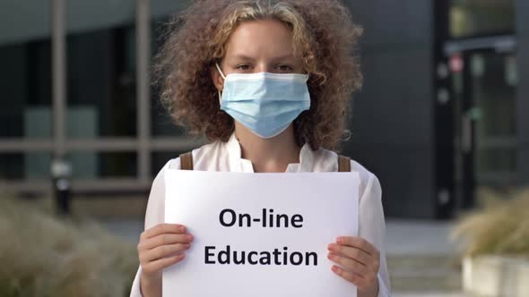 Schoolgirl Wearing a Medical Mask Holds a Sign ONLINE EDUCATION