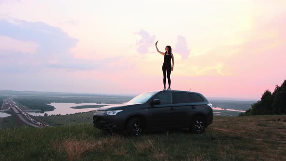 A Young Woman Standing on the Roof of a Car in the Middle of the Field and Trying to Find a Phone