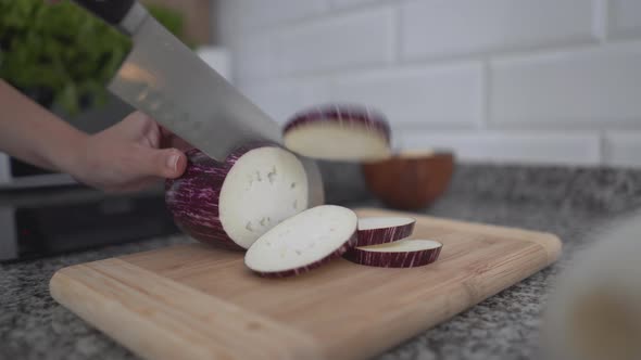 Woman Slicing Eggplant Into Circle Beside Electric Stovetop In The Kitchen