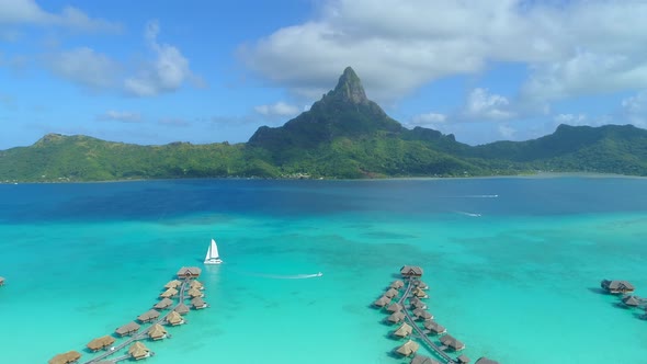 Aerial drone view of a luxury resort, overwater bungalows and sailboat in Bora Bora tropical island