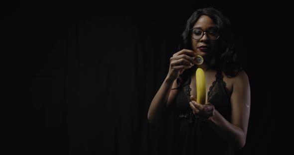 Young Beautiful Woman in Glasses Is Showing How To Use a Condom on a Banana