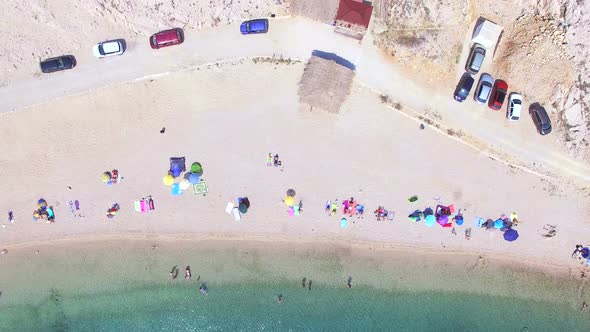 Flying above parked cars and people on sandy beach of Pag island alt