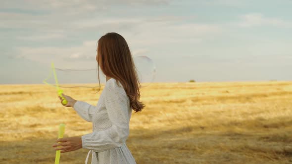 Woman Blows Soap Bubbles Against the Background of a Wheat Field