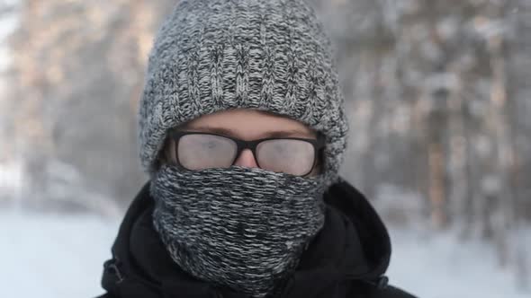 man with misted glasses  in winter snow forest. knitted hat and scarf.