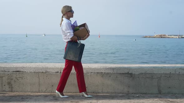 Sad Elegant Businesswoman Walking in Slow Motion with Box Looking at Mediterranean Sea at Background